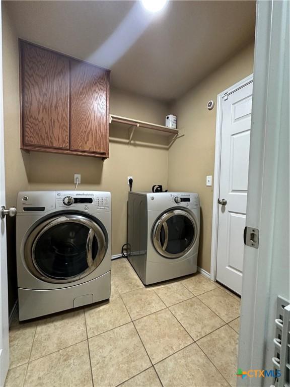 clothes washing area featuring light tile patterned flooring, independent washer and dryer, cabinet space, and baseboards