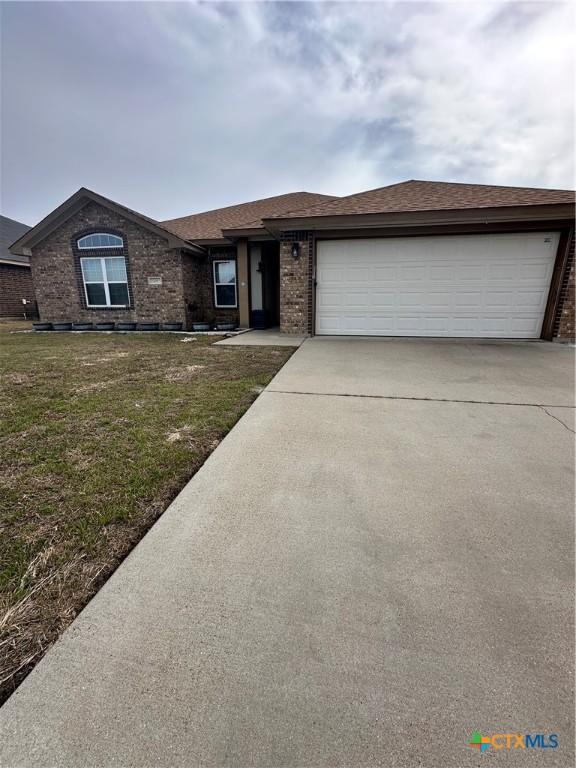 view of front of house with driveway, brick siding, roof with shingles, an attached garage, and a front yard