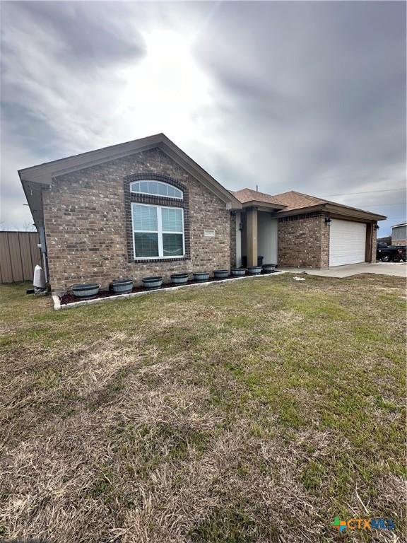 view of front facade featuring an attached garage, concrete driveway, brick siding, and a front yard