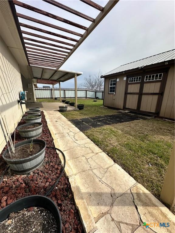 view of yard featuring fence, a pergola, and an outbuilding