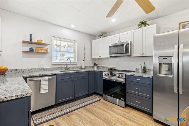 kitchen with a sink, a ceiling fan, white cabinets, appliances with stainless steel finishes, and light wood finished floors