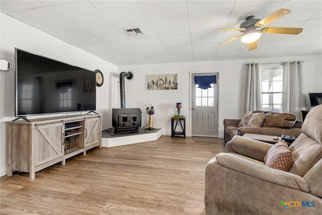 living room with ceiling fan, a wood stove, light wood finished floors, and visible vents