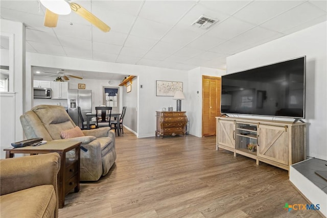 living room featuring baseboards, ceiling fan, visible vents, and wood finished floors