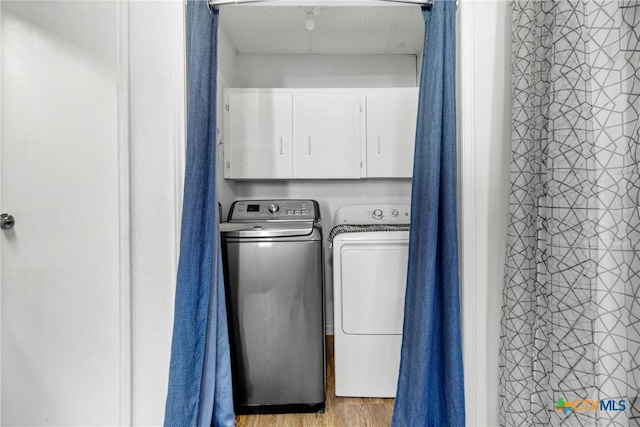 laundry room featuring cabinet space, light wood-style floors, and washing machine and clothes dryer