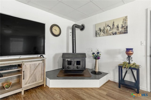 interior details featuring a drop ceiling, wood finished floors, a wood stove, and baseboards