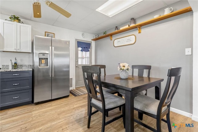 dining area with light wood finished floors, a ceiling fan, a paneled ceiling, and baseboards