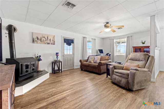 living room featuring a wood stove, light wood finished floors, visible vents, and a drop ceiling