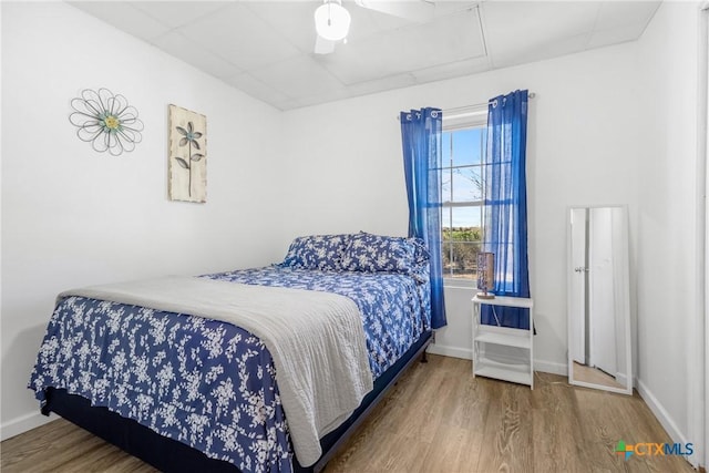 bedroom featuring a drop ceiling, ceiling fan, baseboards, and wood finished floors