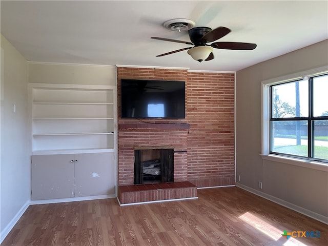 unfurnished living room featuring a brick fireplace, hardwood / wood-style flooring, ceiling fan, and built in shelves