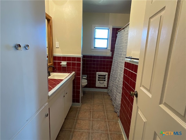 bathroom with vanity, heating unit, toilet, and tile walls