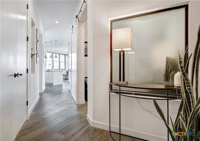 corridor featuring a barn door, baseboards, wood finished floors, and recessed lighting