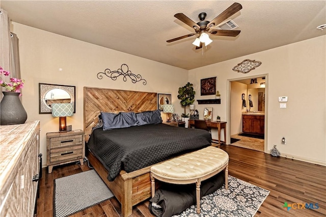 bedroom with a textured ceiling, ceiling fan, dark hardwood / wood-style flooring, and connected bathroom