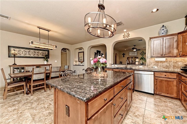 kitchen with stainless steel dishwasher, sink, hanging light fixtures, ceiling fan with notable chandelier, and a center island