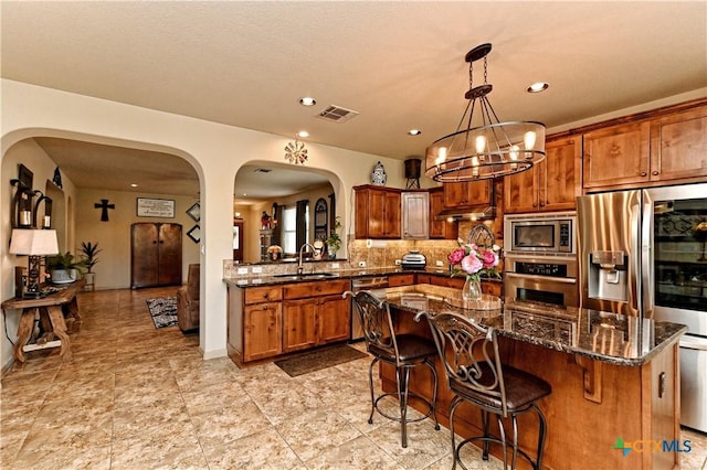 kitchen with decorative light fixtures, stainless steel appliances, dark stone countertops, an inviting chandelier, and sink