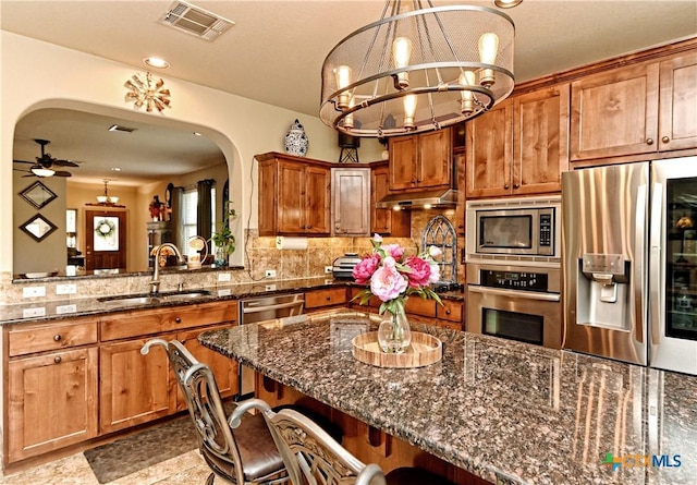 kitchen with a breakfast bar, sink, stainless steel appliances, and dark stone countertops