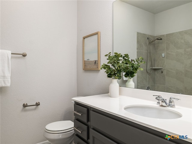 bathroom featuring toilet, a tile shower, and vanity