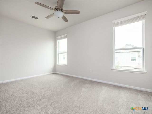 carpeted spare room featuring a ceiling fan, visible vents, and baseboards