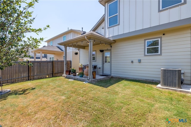 rear view of property with a patio, central AC unit, fence, a yard, and board and batten siding