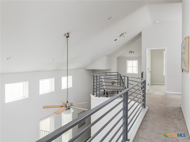 hallway with high vaulted ceiling, light carpet, visible vents, an upstairs landing, and baseboards