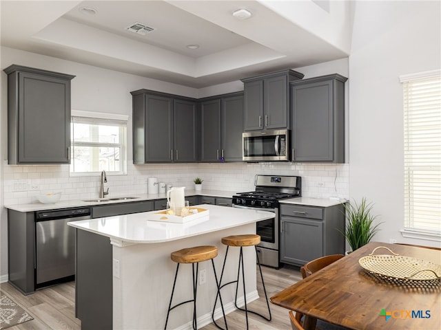 kitchen with visible vents, a tray ceiling, stainless steel appliances, light wood-style floors, and a sink