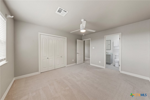 unfurnished bedroom featuring multiple windows, ensuite bath, light carpet, and ceiling fan