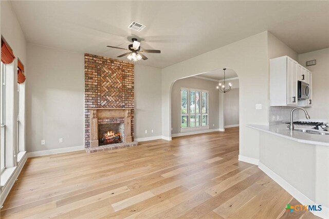 4512 Sunflower Ln, Temple, TX 76502 - unfurnished living room with arched walkways, a ceiling fan, a sink, light wood-type flooring, and a fireplace