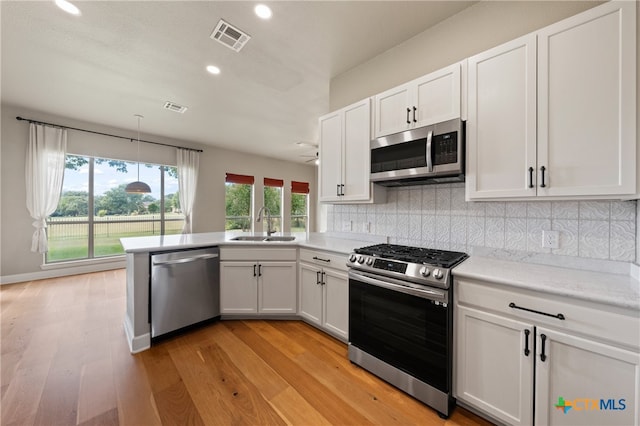 kitchen featuring stainless steel appliances, white cabinetry, light wood-type flooring, and decorative backsplash