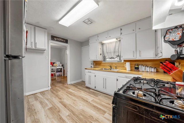 kitchen with stainless steel fridge, black gas range oven, ventilation hood, sink, and white cabinets