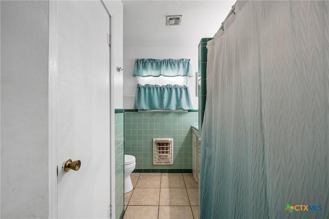 bathroom featuring curtained shower, tile patterned flooring, heating unit, toilet, and tile walls