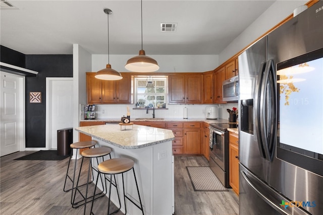 kitchen featuring stainless steel appliances, decorative light fixtures, sink, hardwood / wood-style flooring, and a center island