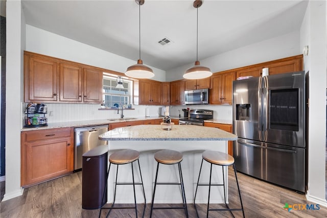 kitchen featuring wood-type flooring, sink, a kitchen island, pendant lighting, and appliances with stainless steel finishes