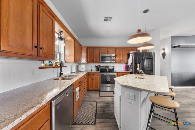 kitchen with stainless steel appliances, sink, light stone counters, dark hardwood / wood-style floors, and a breakfast bar area