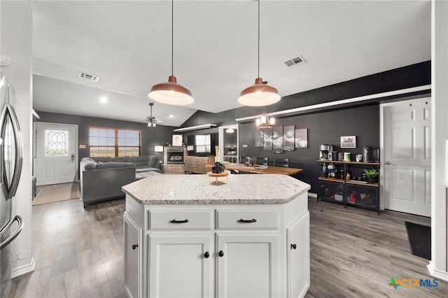 kitchen featuring hanging light fixtures, hardwood / wood-style floors, vaulted ceiling, white cabinets, and a center island