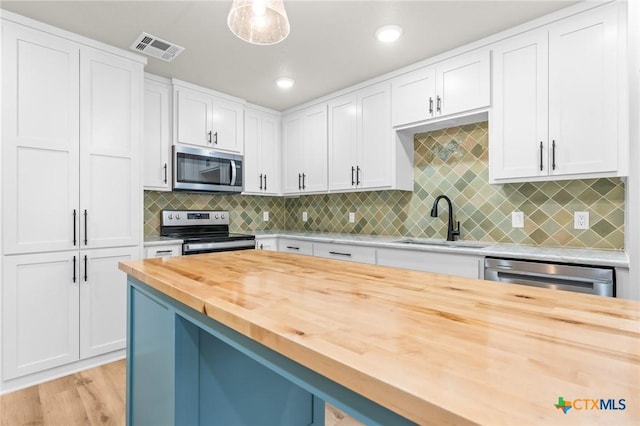 kitchen featuring stainless steel appliances, white cabinetry, and wooden counters