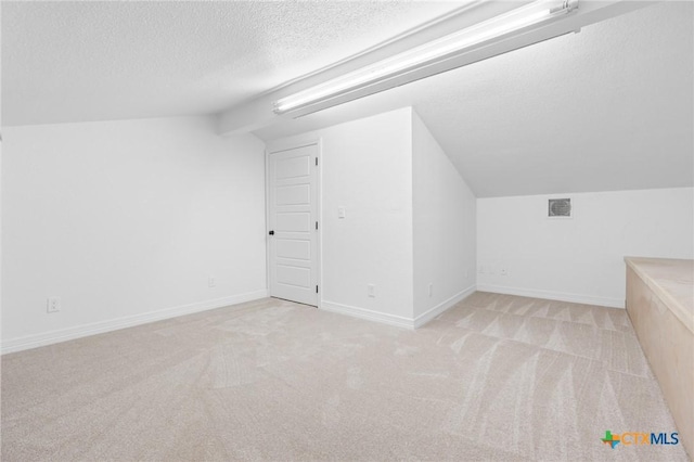 additional living space with a textured ceiling, vaulted ceiling, and light carpet