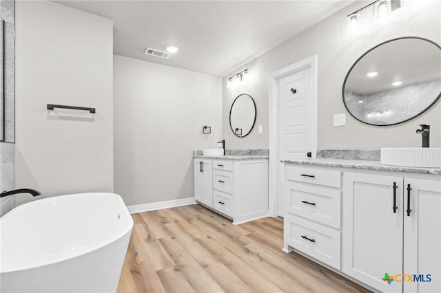 bathroom with a textured ceiling, hardwood / wood-style flooring, a tub, and vanity