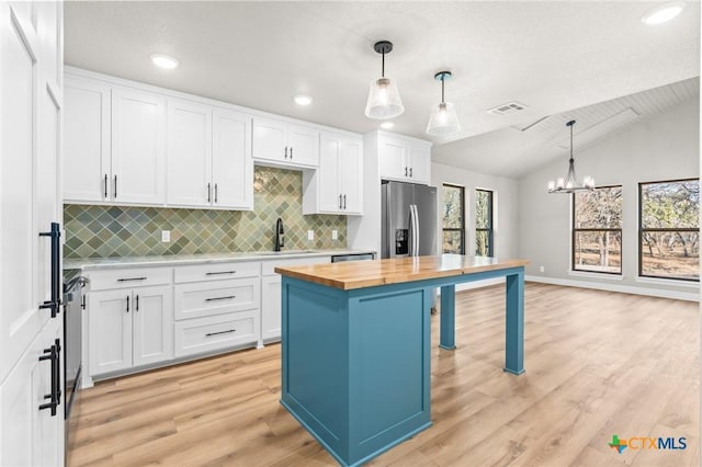 kitchen with a center island, pendant lighting, white cabinets, stainless steel fridge, and wood counters