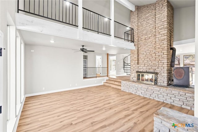 unfurnished living room with ceiling fan, a fireplace, a towering ceiling, beamed ceiling, and light hardwood / wood-style flooring