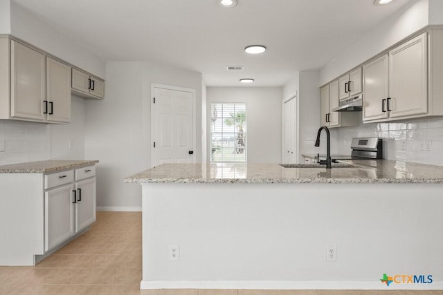 kitchen with light stone countertops, sink, kitchen peninsula, and tasteful backsplash