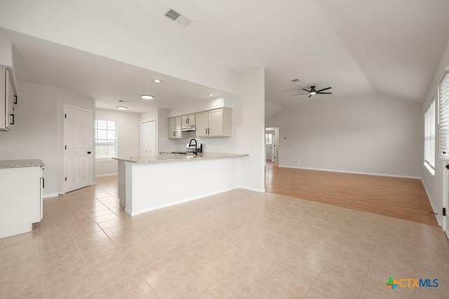 kitchen featuring light stone countertops, vaulted ceiling, kitchen peninsula, light tile patterned flooring, and ceiling fan