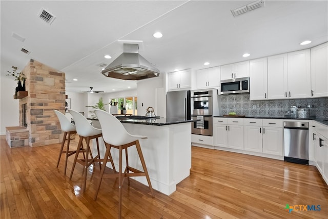 456 Magazine Ave, New Braunfels, TX 78130 - kitchen featuring island range hood, appliances with stainless steel finishes, a breakfast bar area, dark countertops, and light wood-style flooring