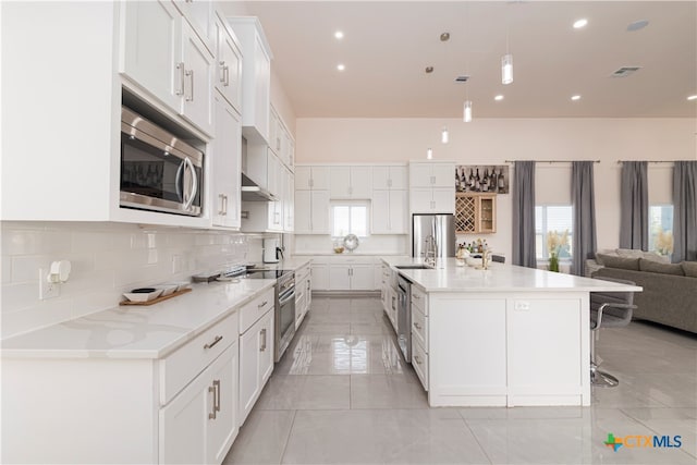 kitchen with white cabinets, appliances with stainless steel finishes, a large island with sink, and pendant lighting