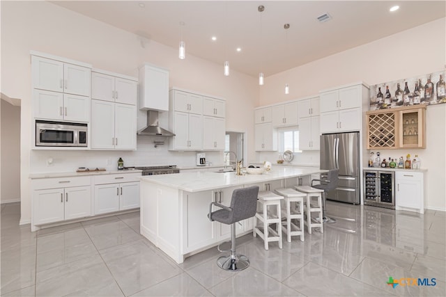 kitchen with white cabinetry, appliances with stainless steel finishes, wall chimney exhaust hood, a breakfast bar area, and a kitchen island with sink