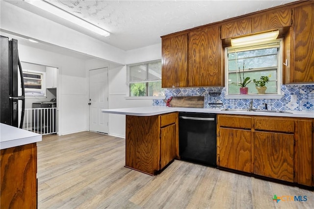 kitchen featuring light wood-type flooring, a sink, black appliances, and light countertops