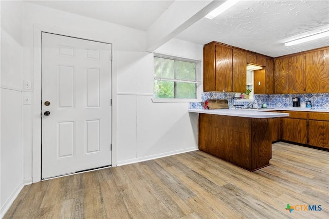 kitchen featuring brown cabinets, light countertops, a peninsula, light wood-type flooring, and tasteful backsplash