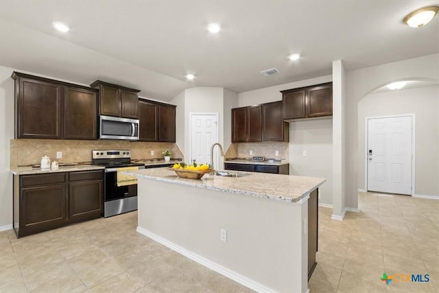 kitchen with light stone countertops, sink, tasteful backsplash, an island with sink, and appliances with stainless steel finishes