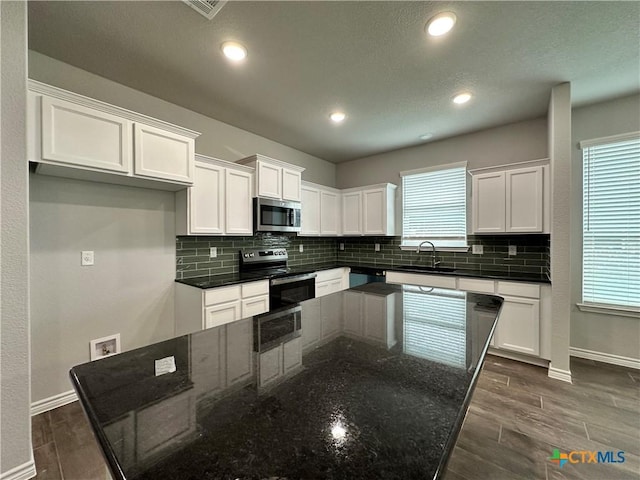 kitchen with white cabinets, appliances with stainless steel finishes, dark stone countertops, and sink