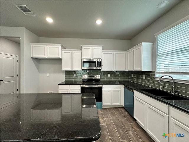 kitchen featuring sink, decorative backsplash, dark stone countertops, white cabinetry, and stainless steel appliances