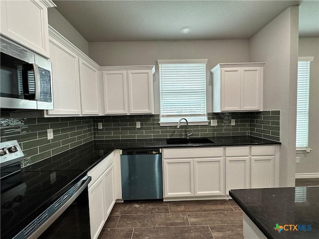 kitchen with sink, plenty of natural light, dark stone counters, white cabinets, and appliances with stainless steel finishes