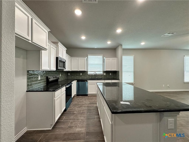 kitchen featuring white cabinetry, sink, dark stone counters, a kitchen island, and appliances with stainless steel finishes